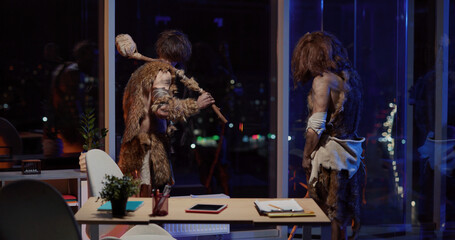 Primeval couple of two savages with prehistoric tools standing in corporate modern office looking out of window celebrating successful timetravel.