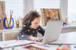 © boytsov - Cute small child girl sitting at the table in earphones seriosly doing homework or online schooling using laptop. Homeschooling or remote classes concept. High quality photo