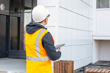 Builder inspects the new building, writing down comments in the tablet.. Building inspector. Construction site check drawing and business workflow of new high rise house.