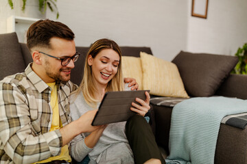 Couple shopping online, making order with digital tablet while sitting at home floor.