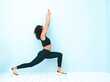 © halayalex - Portrait of fitness smiling black woman in sports clothing with afro curls hairstyle.She wearing sportswear.Young beautiful model stretching out before training.Female sitting in studio near blue wall