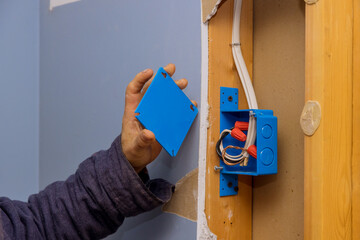 Hands of an electrician fasten the electrical box to the beams to place