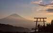 Late afternoon view of a torii gate and Mount Fuji under a partly-cloudy blue and yellow sunset sky