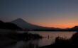 Early evening view of Mount Fuji and Lake Kawaguchi under a thin crescent moon, with a lone fisherman visible near the shore