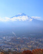 Daytime view of Mount Fuji from afar, partially covered by low clouds under a bright blue sky and with part of the city of Fujiyoshida visible