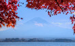 Hazy daytime view of Mount Fuji and Lake Kawaguchi, framed by red maple leaves and under a blue sky