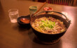 A bowl of houtou noodles and accompanying tableware on a wooden table inside a restaurant
