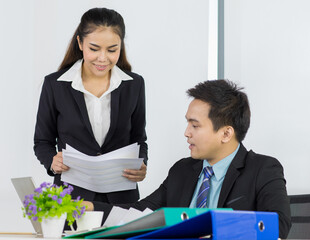 Asian office people are secretary smiling and holding document paper for presentation to boss manager while sitting and looking paper document on her hand in office place