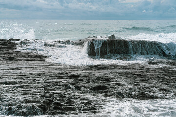 Waves crashing over black rocks in frozen motion on a warm sunny summer day. Blue and white sea colors. Rainbow Bay, Gold Coast, Queensland, Australia.