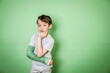 © epiximages - cool young schoolboy with broken arm and green arm plaster posing in front of green background