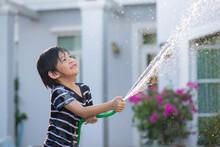 Asian Boy Has Fun Playing In Water From A Hose Outdoors