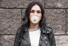 Beautiful Brunette Woman With Curly Hair Inflates A Bubble Gum Ball On The Street