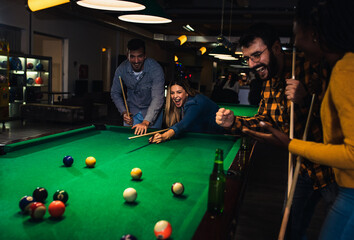 Wall Mural - Four smiling friends in bar playing billiard together.