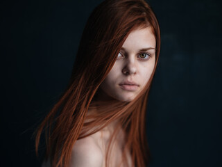 Close-up cropped view of a woman with red hair looking forward on a black background