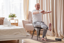 Elderly Man Practicing Yoga Asana Or Sport Exercise For Legs And Hands On Chair