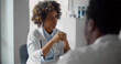 © nimito - African-american woman doctor sitting at table and talking to male colleague in office