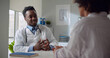 © nimito - Afro-american male doctor talking to patient sitting at desk in office.