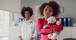 © nimito - Portrait of little african girl holding teddy bear with young female doctor standing on background