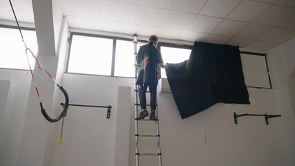 Video production gaffer climb ladder to block window sunlight with black fill