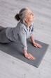 © LIGHTFIELD STUDIOS - pleased middle aged woman in cobra pose practicing yoga on mat at home