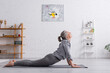 © LIGHTFIELD STUDIOS - side view pleased middle aged woman in cobra pose practicing yoga on mat at home