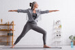 © LIGHTFIELD STUDIOS - middle aged woman in sportwear standing in warrior pose while practicing yoga at home