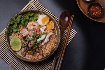 Wall Mural - Instant noodles with seafood tom yum, prawns, squid, mussels in a brown ceramic bowl Close up