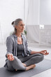 © LIGHTFIELD STUDIOS - mature woman with grey hair sitting in lotus pose while meditating on yoga mat
