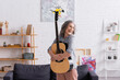 © LIGHTFIELD STUDIOS - cheerful mature woman with grey hair embracing acoustic guitar near couch in living room
