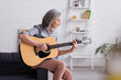 © LIGHTFIELD STUDIOS - mature woman with grey hair playing acoustic guitar in living room