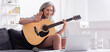 © LIGHTFIELD STUDIOS - middle aged woman with grey hair holding acoustic guitar while waving hand during video call on laptop, banner