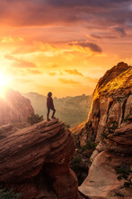 Adventurous Woman At The Edge Of A Cliff Is Looking At A Beautiful Landscape View In The Canyon. Sunset Sky Art Render. Taken In Zion National Park, Utah, United States.
