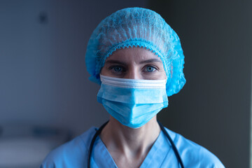 Portrait of caucasian female doctor in hospital wearing face mask, medical cap and scrubs