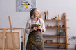 © LIGHTFIELD STUDIOS - middle aged artist in apron holding paintbrush near easel