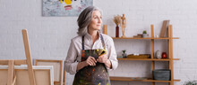 Middle Aged Artist In Apron Holding Paintbrush Near Easel, Banner
