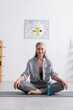 © LIGHTFIELD STUDIOS - happy middle aged woman sitting in lotus pose on yoga mat