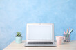 © New Africa - Modern laptop with blank screen, cup and office supplies on white table near light blue wall. Space for text