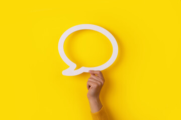 hand holding dialogue bubble over yellow background