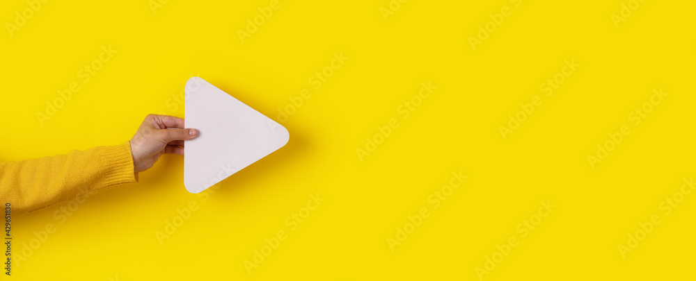 hand holding media player button icon over trendy yellow background, panoramic layout - obrazy, fototapety, plakaty 