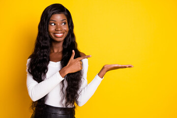 Sticker - Photo portrait of girl with long hair curious pointing holding on hand empty space isolated vivid yellow color background