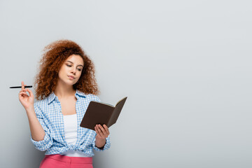 Wall Mural - thoughtful woman in plaid shirt holding pen and notebook on grey background