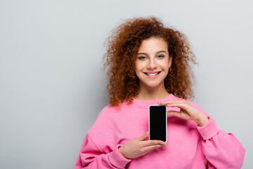 Wall Mural - joyful woman showing smartphone with blank screen isolated on grey