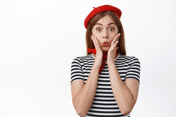 Wall Mural - Close up of excited and surprised cute girl winning something, holding hands on cheeks and look fascinated, receive gift, standing amazed against white background