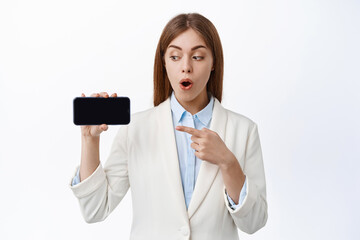 Wall Mural - Professional office ceo woman points at empty cellphone screen, shows application or website page on phone, white background