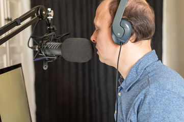 An author wearing headphones is recording a video course at home using a microphone and his computer