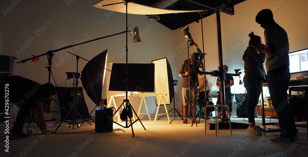 Behind the shooting video production and film crew team. Silhouette of people in studio setting camera and lighting for shooting online video. Film production concept. - obrazy, fototapety, plakaty 