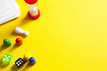 Layout of board games on a yellow background: dice, chips, hourglass timer. Entertainment at home for children and adults. Copy space