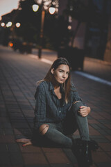 Poster - Young Caucasian female wearing a shirt and ripped jeans sitting on the road