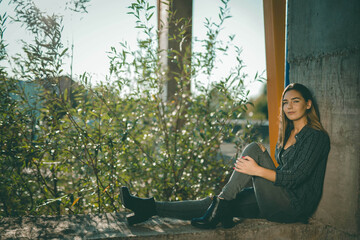 Sticker - Young Caucasian female wearing a shirt and ripped jeans sitting on a concrete wall