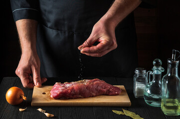 Wall Mural - The chef sprinkles raw meat with salt. Preparing beef meat before baking. Working environment in the kitchen of restaurant or cafe